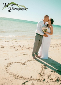 Bride Rachel and Groom Phill kissing next to a heart drawn in the sand at the beach