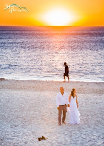 Bride and groom standing on the beach with a sunset behind them