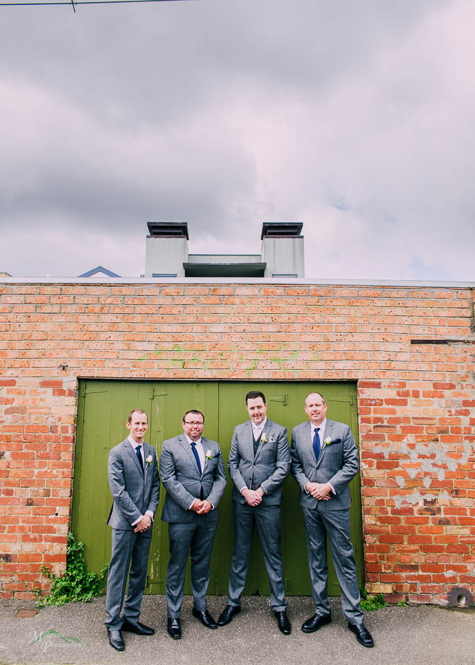 Groomsmen by an iron door and brick wall