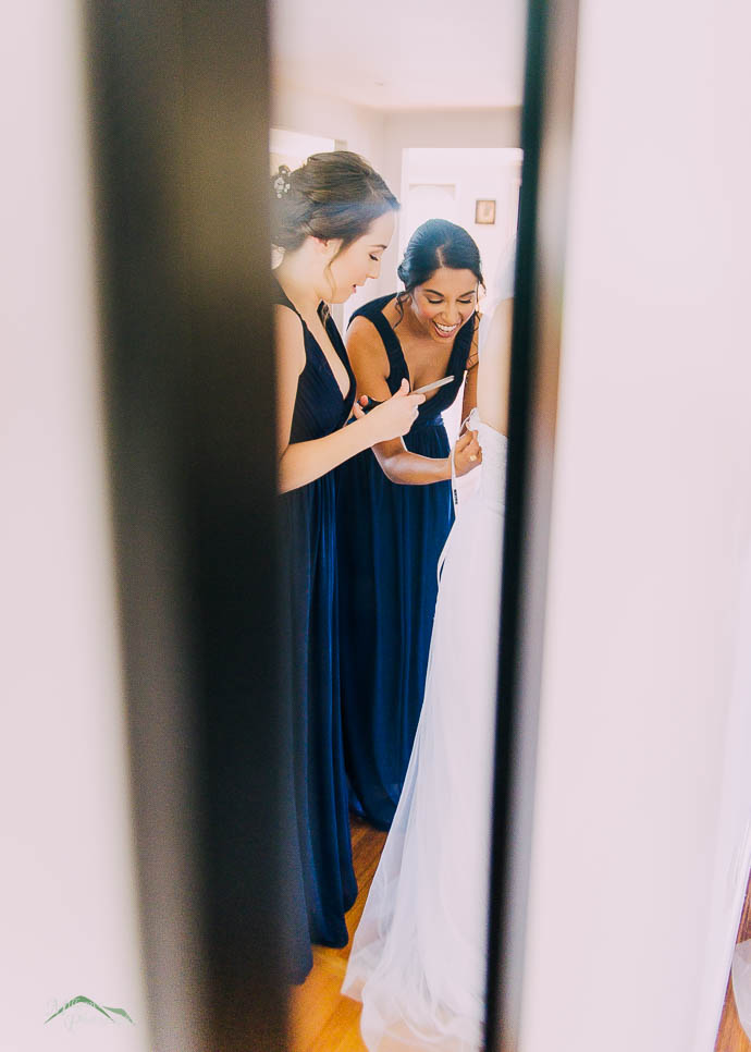 Bridesmaids in mirror, doing up dress