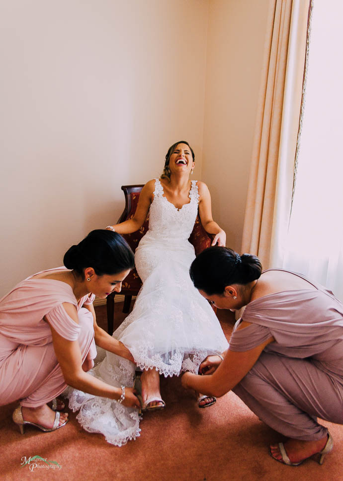 Bride laughing while bridesmaids put her shoes on