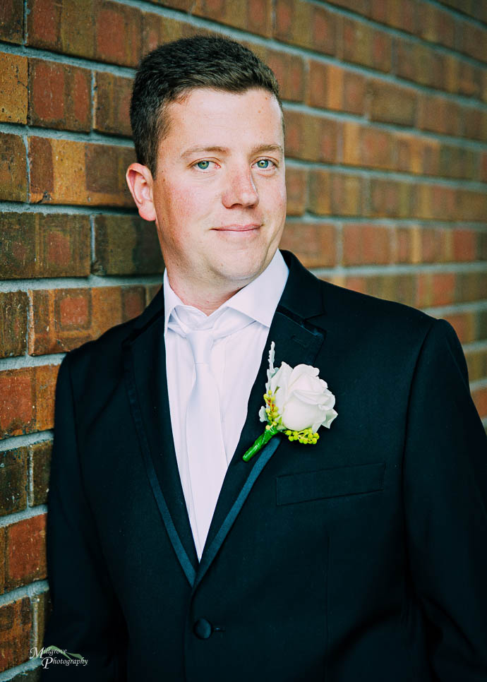 Groom leaning against a brick wall
