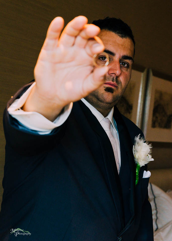 Groom holding wedding ring in front of his eye and looking throu