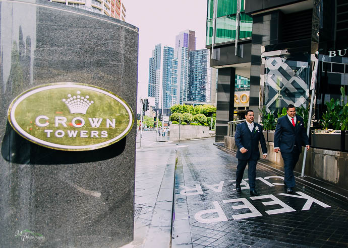 Groom and groomsman walking past Crown Towers