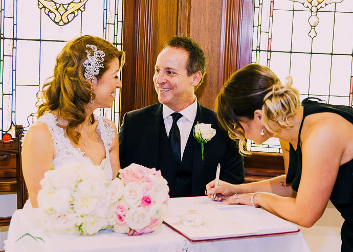 Bride and groom smiling while bridesmaid sign register