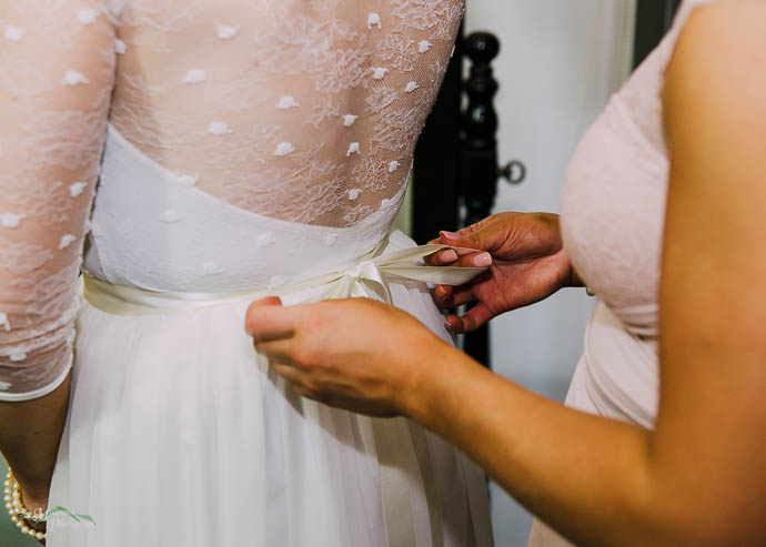 Bridesmaid adjusting ribbon on bride's dress