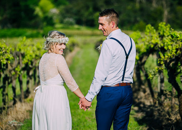 Bride and groom looking over their shoulders in the vines at Lil