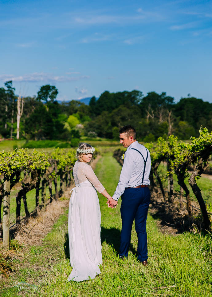 Bride and groom looking over their shoulders in the vines at Lil