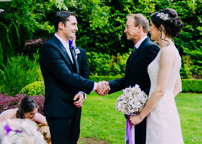 Groom shaking father’s hand while Bride looks on