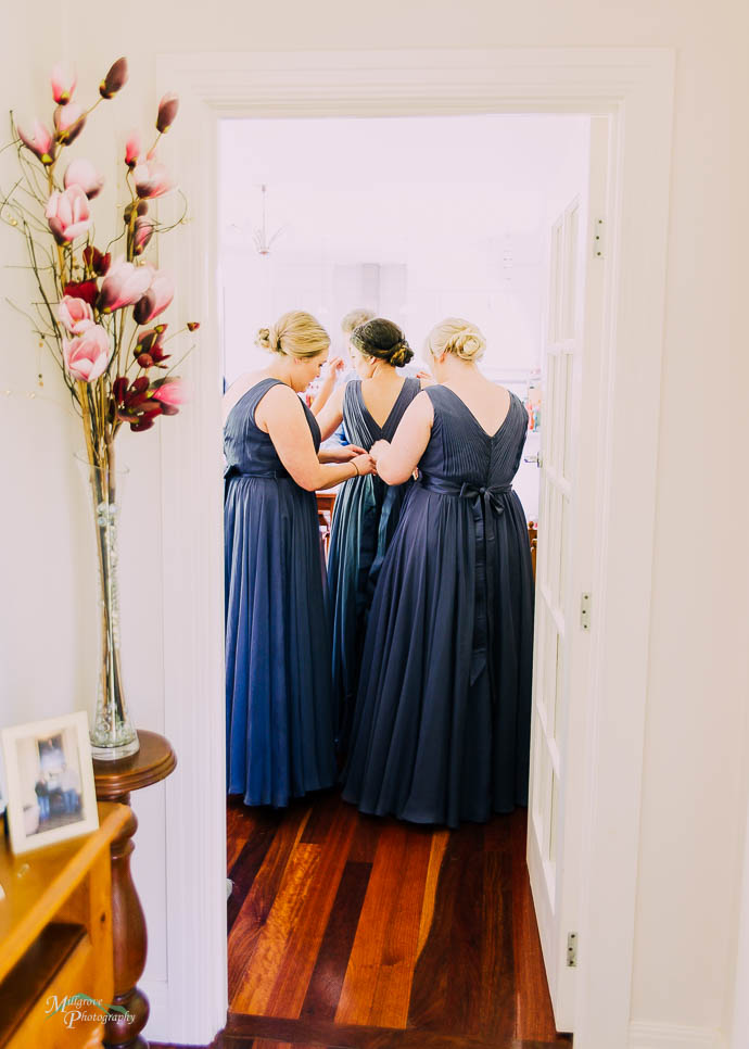 Bridesmaid’s helping each other with their dresses through a doorway