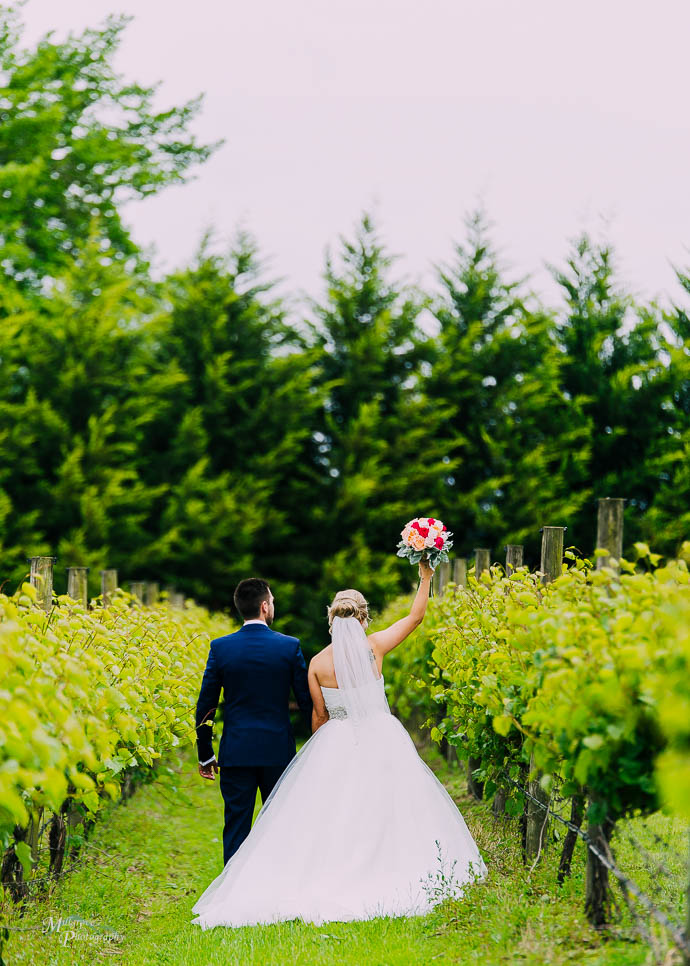 Bride raising her flowers in the air as she walks between the vines at Wild Cattle Creek Winery