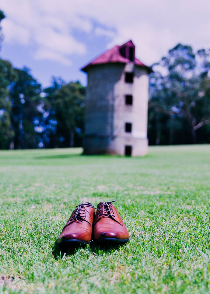 Groom's shoes on the grass with a silo in the background