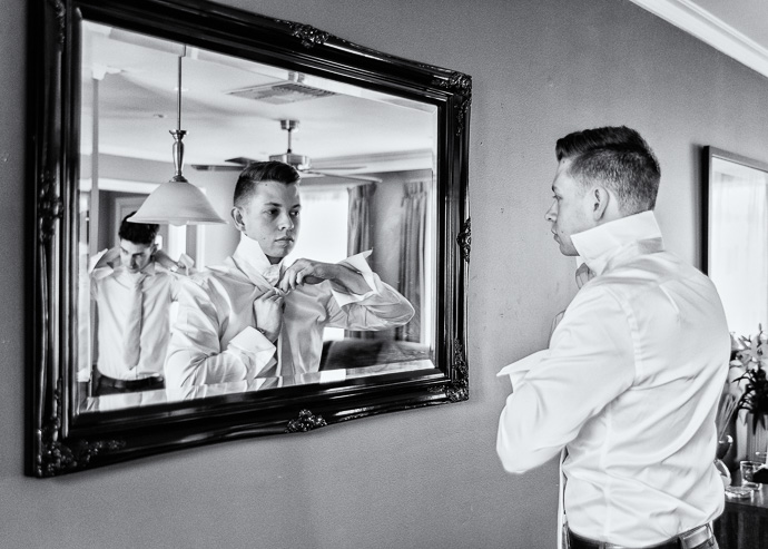 Groom doing up his tie in the mirror