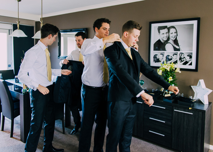 Groomsmen helping groom put jacket on