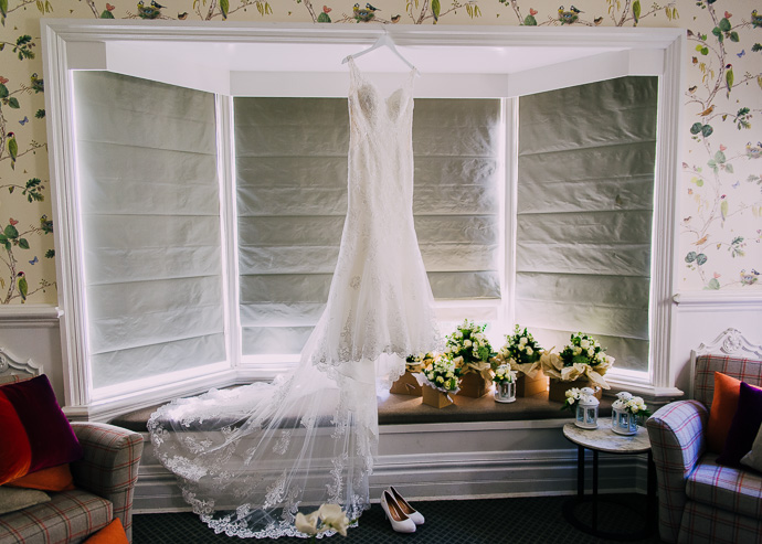 wedding dress hanging next to flowers in a window