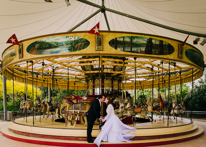 A bride and groom kissing in front of an old carousel