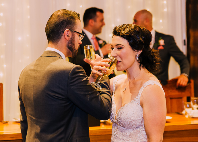 A bride and groom drinking with linked arms