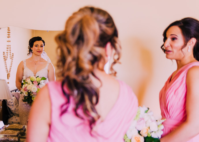 A bride in the mirror with two women in pink dresses