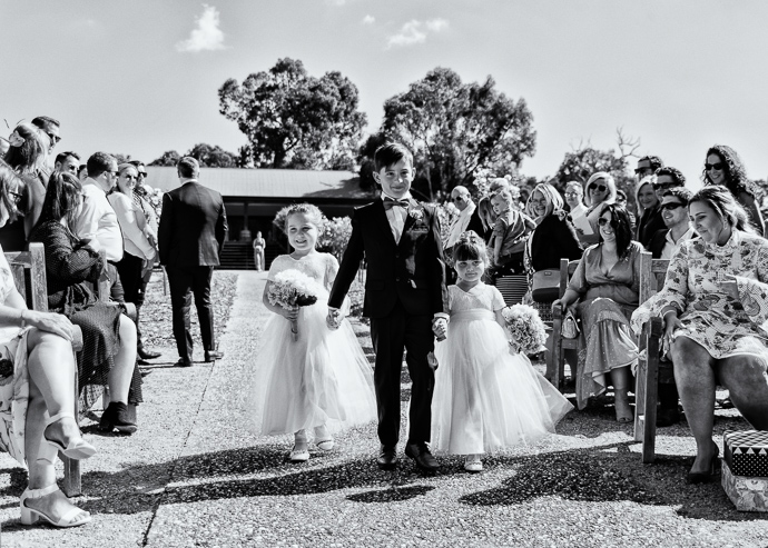 A boy walking tow little girls down the stairs at a wedding, black and white