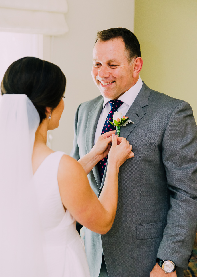 A bride pinning a flower on her father's suit